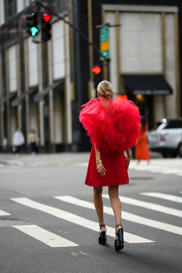 new york, new york september 12 leonie hanne wears gold earrings, a red short dress with oversized ruffled tulle shoulder, a gold juste un clou bracelet from cartier, a gold and silver watch, gold rings, a silver bracelet, a black glitter with gold metallic borders clutch, black shiny varnished leather heels sandals  shoes , outside carolina herrera, during new york fashion week, on september 12, 2022 in new york city photo by edward berthelotgetty images