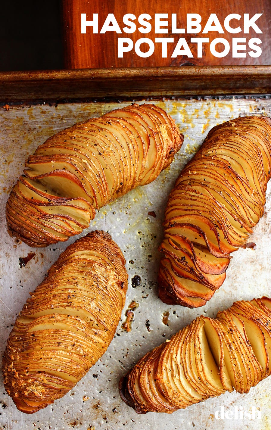 freshly baked hasselback potatoes are golden brown and glistening on a silver sheet tray, topped with black pepper and salt