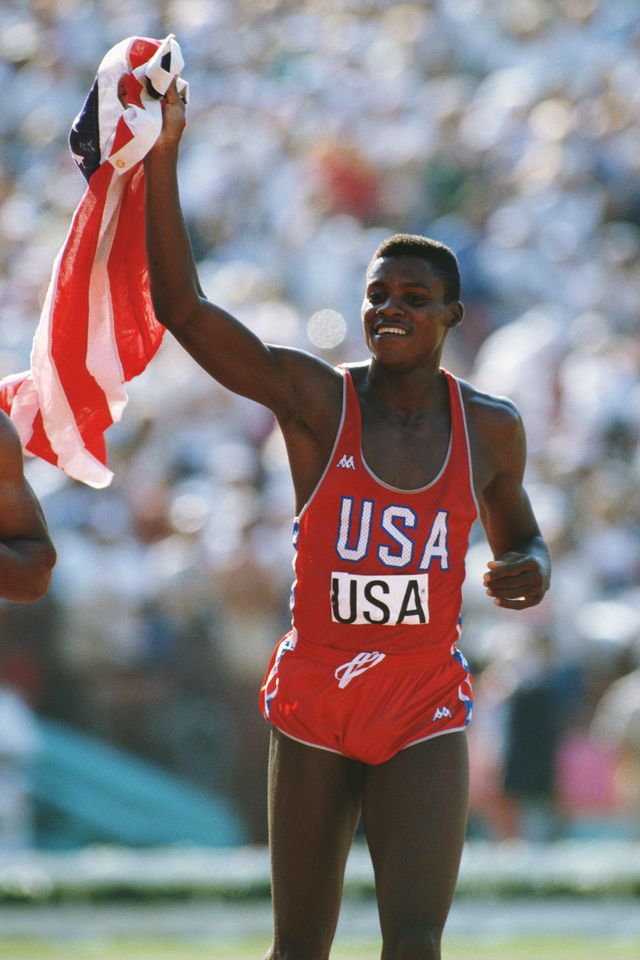 carl lewis in red usa singlet waves american flag at the 1984 los angeles olympic games