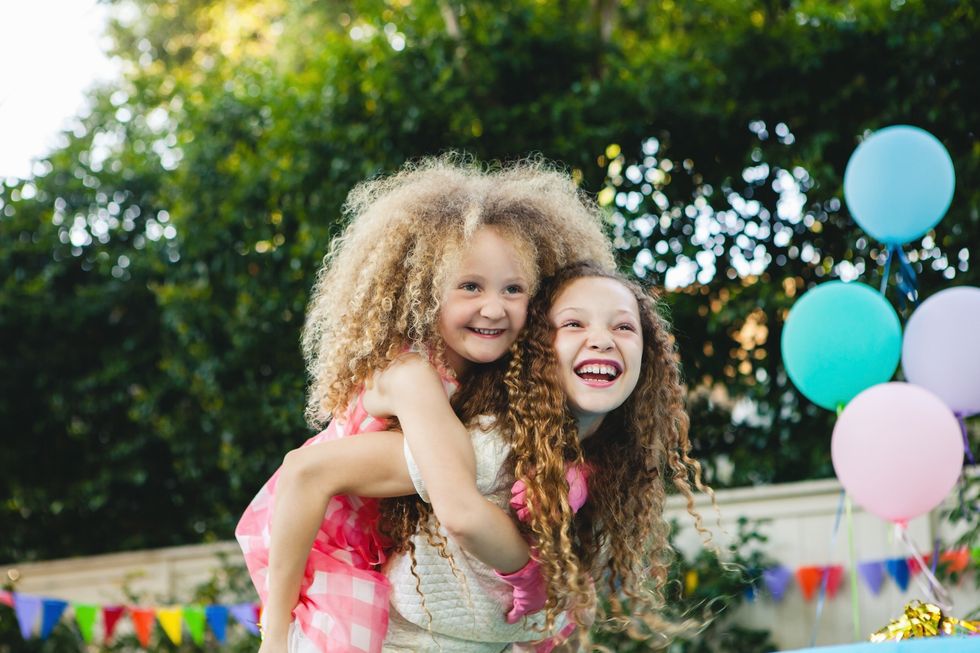 sister giving piggyback ride to sister during birthday party with balloons outdoors