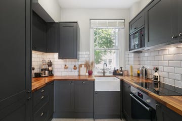 a modern city kitchen with grey cabinets and wooden worktops and a window beyond