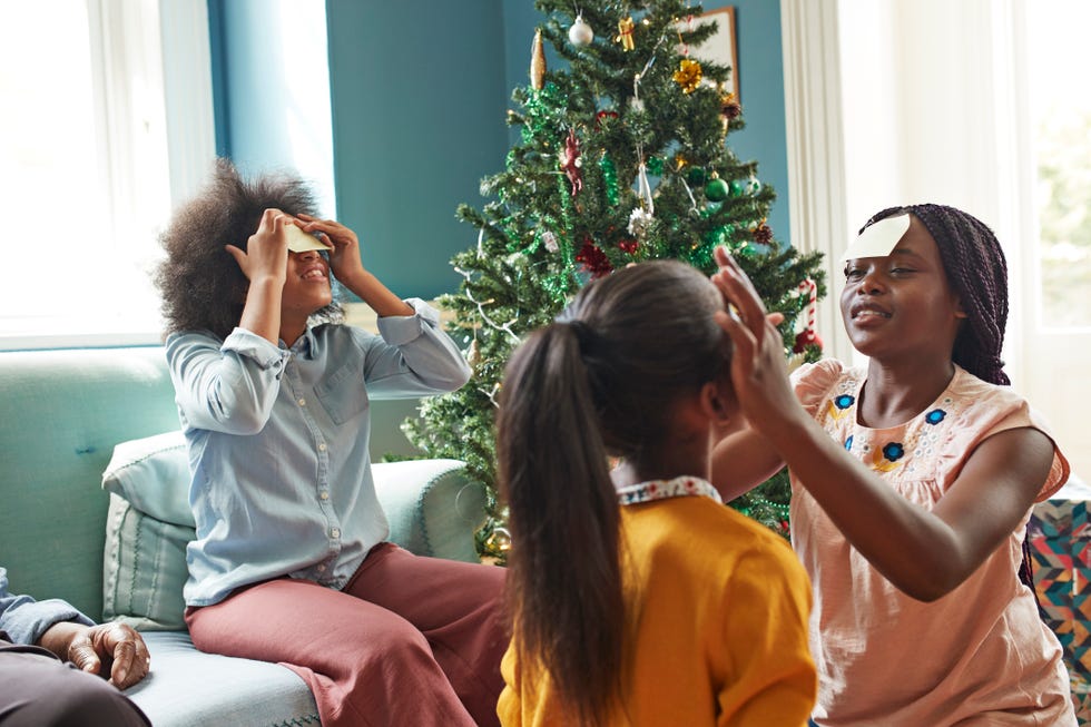 sisters sticking notes on their foreheads at home in front of the christmas tree