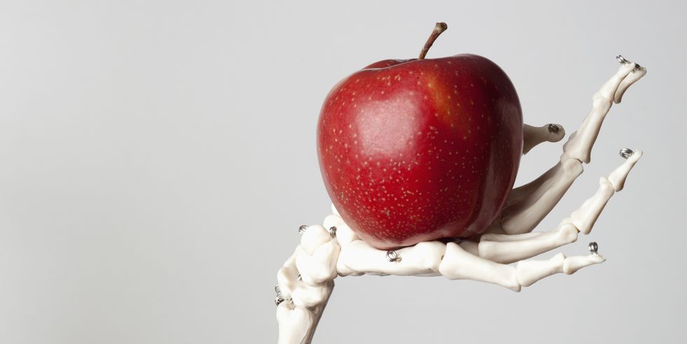 a skeleton arm and hand holding a red apple