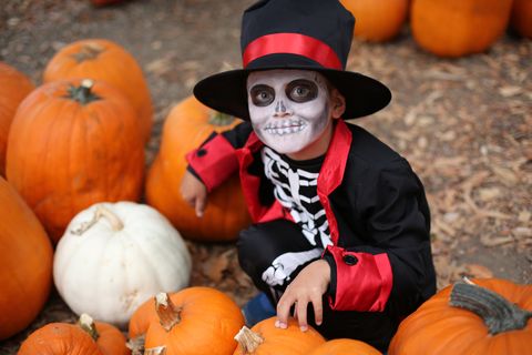 halloween children playing trick or treating boy in halloween costume skeleton with hat and smoking among orange pumpkins halloween children