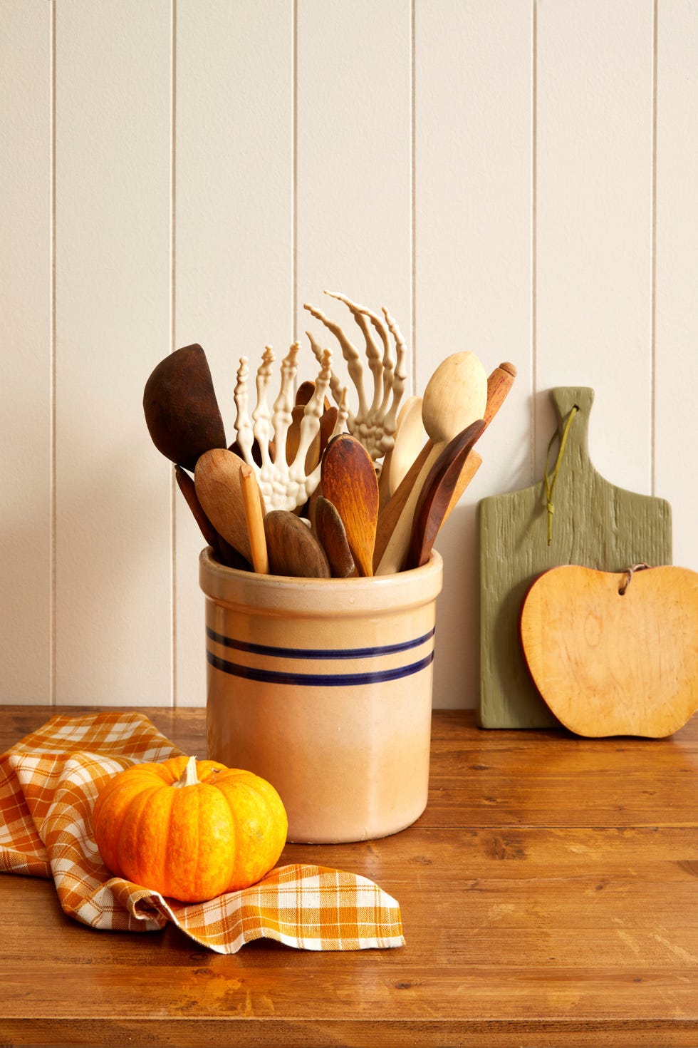 fake skeleton hands tucked into a kitchen crock with wooden spoons set on a kitchen counter