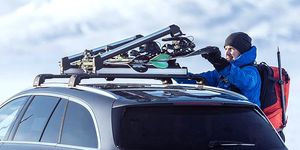 man adjusting snowboard on car roof rack