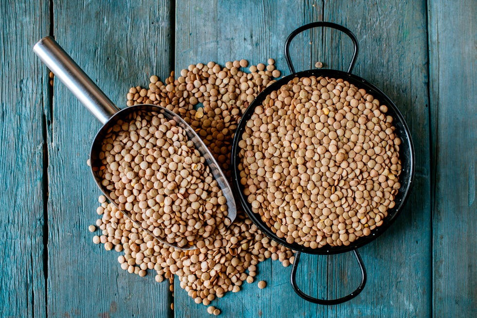 Skillet and metal scoop with dried brown lentils on wood