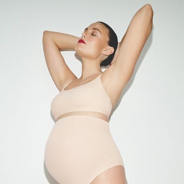 a pregnant person posing with arms raised in a minimalistic setting a pregnant person posing with arms raised in a minimalistic setting