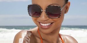 portrait of young woman wearing sunglasses and applying sunscreen at the beach