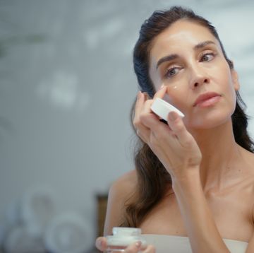 mujer aplicandose crema ante un espejo