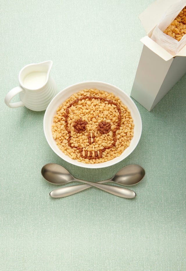 bowl of breakfast cereal with rice krispies styled to look like a skull , with spoons as cross bones, jug of milk,