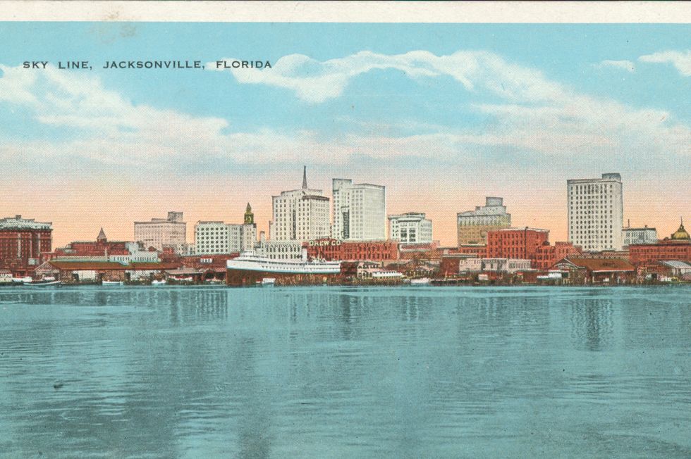 an illustrated skyline of jacksonville florida in 1924 shows many tall buildings and several ships docked at the shore with water in the foreground