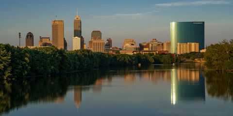 skyline view at sunset into dusk of indianapolis buildings on white river reflect in water, indiana