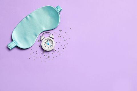 sleeping mask, alarm clock and confetti on purple background