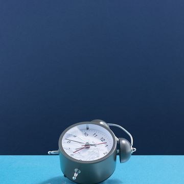 a smashed alarm clock laying on its side, broken glass two tone blue background
