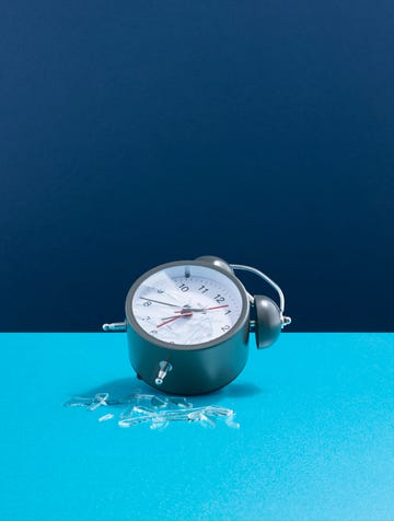 a smashed alarm clock laying on its side, broken glass two tone blue background