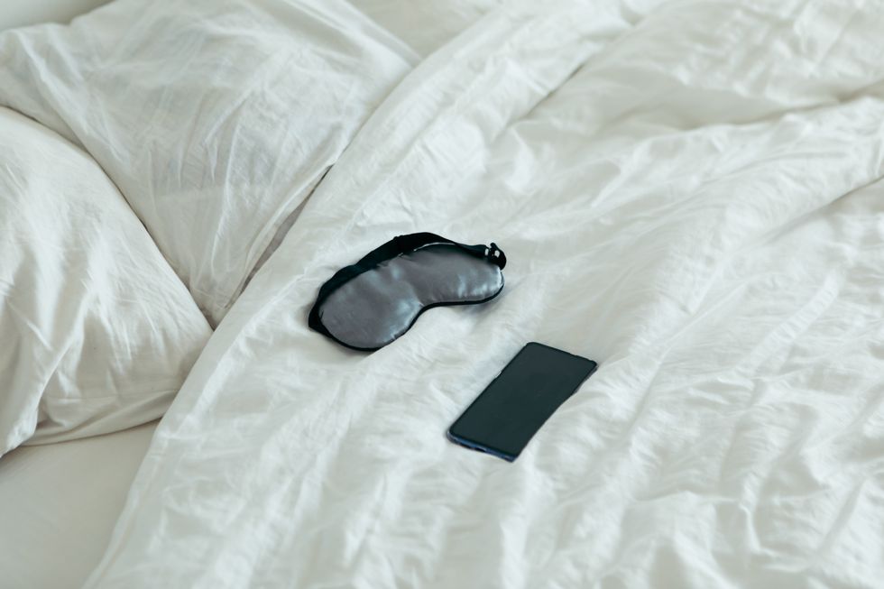 sleeping mask with phone at bed with white sheets sunny morning bedroom
