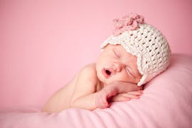 sleeping newborn baby girl wearing a crocheted hat on pink