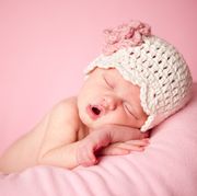 sleeping newborn baby girl wearing a crocheted hat on pink