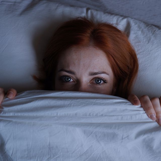 sleepless woman lying in bed hiding under duvet at night