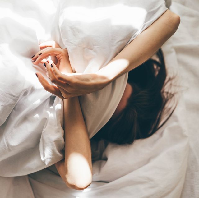 sleepless woman lying in bed hiding under duvet