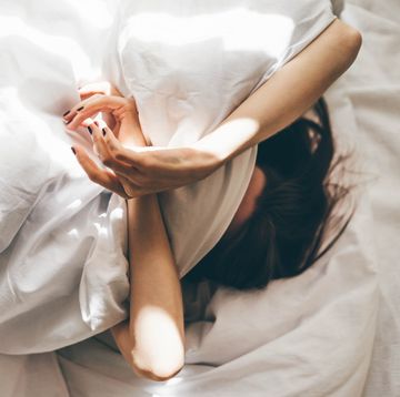 sleepless woman lying in bed hiding under duvet