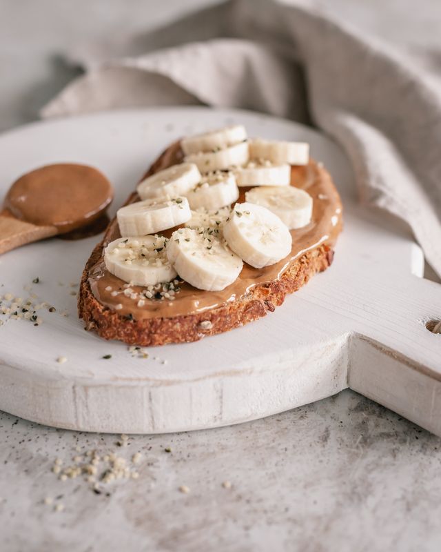 slice of sourdough bread with peanut butter, banana and hemp seeds on a chopping board