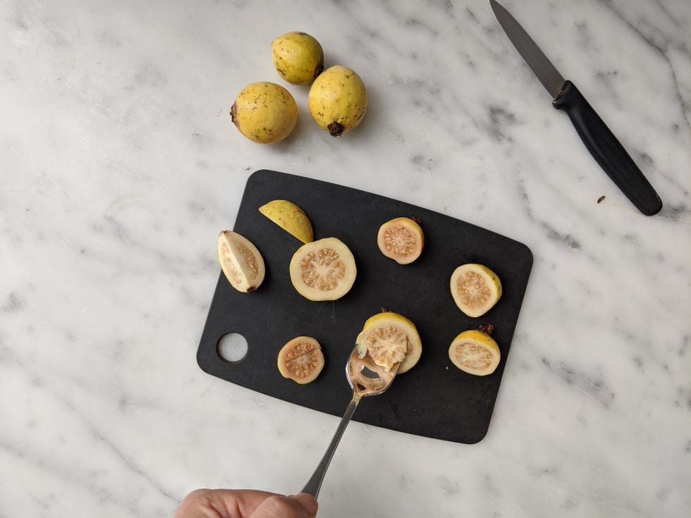 sliced baby guava on a cutting board, one shown being scooped out with a spoon