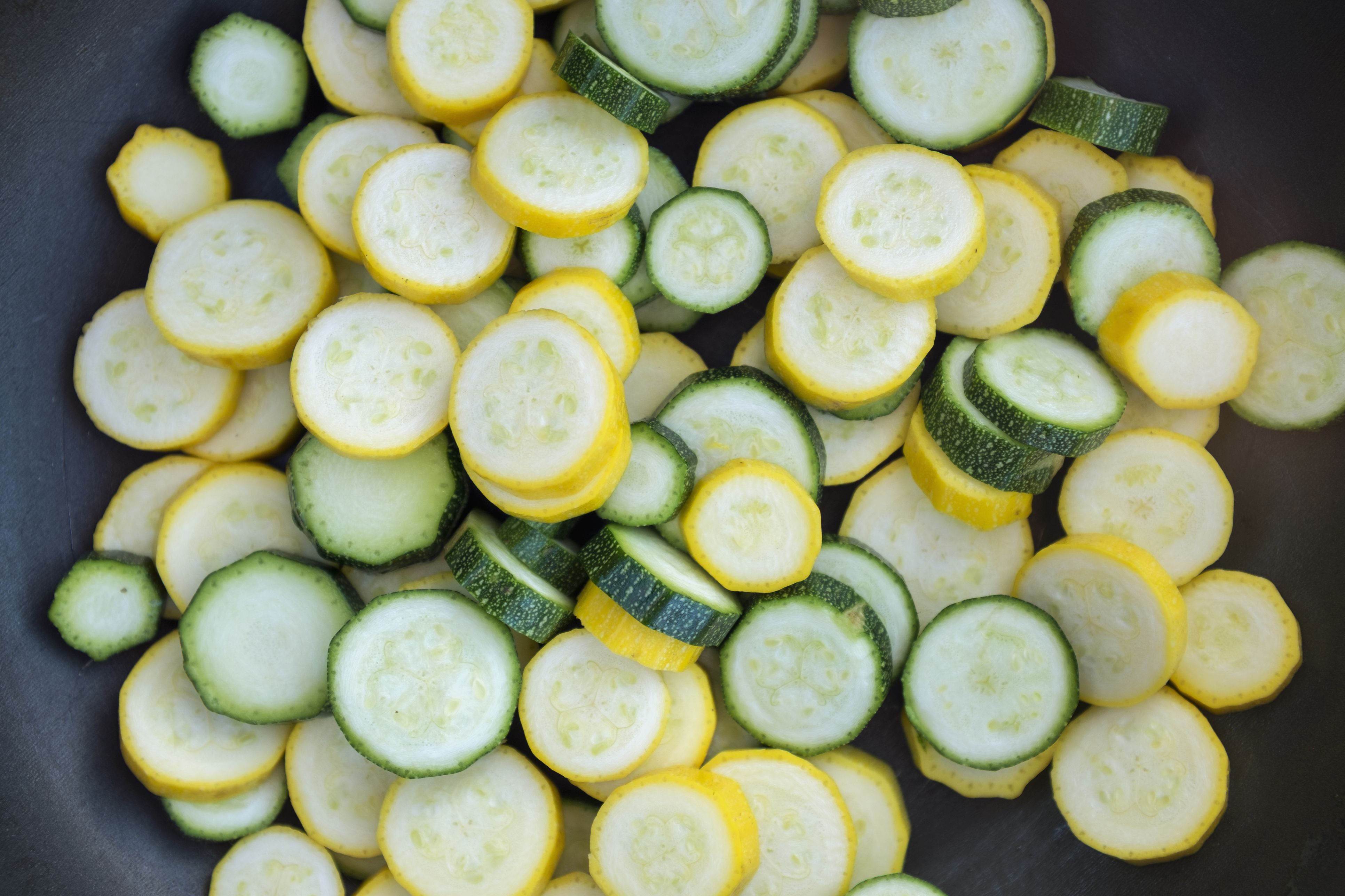 Sliced fresh zucchini courgette vegetables with green and yellow skins in a frying pan.