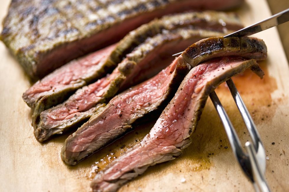 Sliced steak on cutting board with carving utensils, close-up