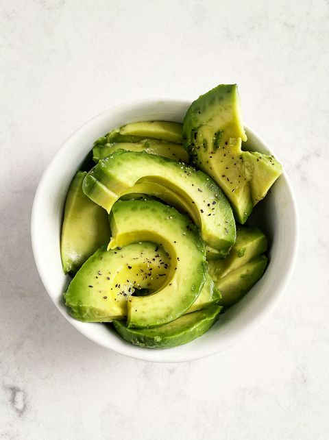 slices of fresh avocado in a bowl on white, marble background