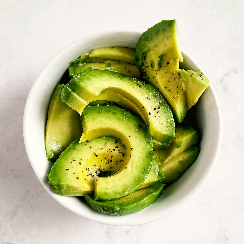 slices of fresh avocado in a bowl on white, marble background