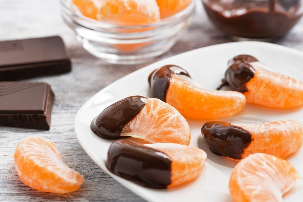 slices of tangerine in chocolate served on a white plate, white wooden textured background