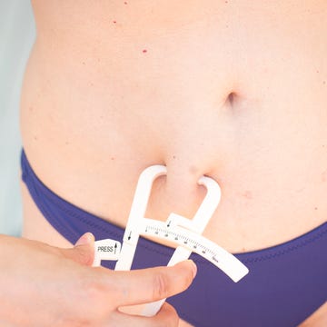 Slim attractive young lady wearing bikini in summer using fat caliper to measure bodyfat. meting van lichaamsvetpercentage