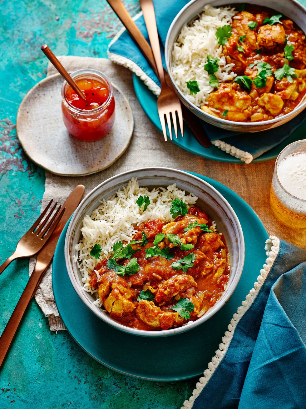 two bowls of chicken curry with rice and a jar of chutney