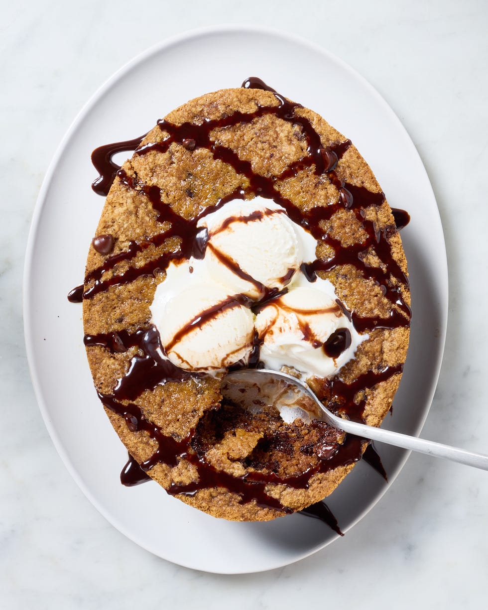 large chocolate chip cookie topped with vanilla ice cream and drizzled with chocolate sauce on top of a white platter