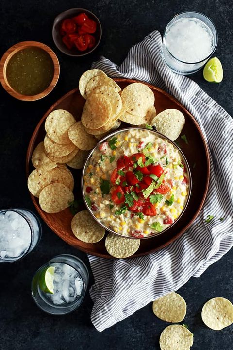slow cooker salsa verde corn dip in bowl on wooden tray with chips and drinks