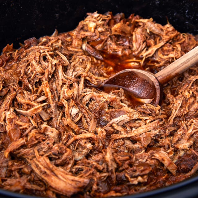 shredded bbq pulled pork in a slow cooker with a wooden spoon