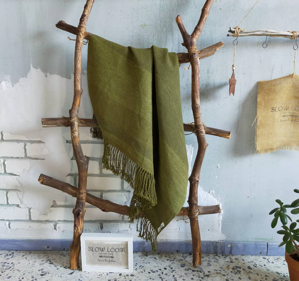 chal de lino verde de slow loom colgado sobre un perchero de palos naturales