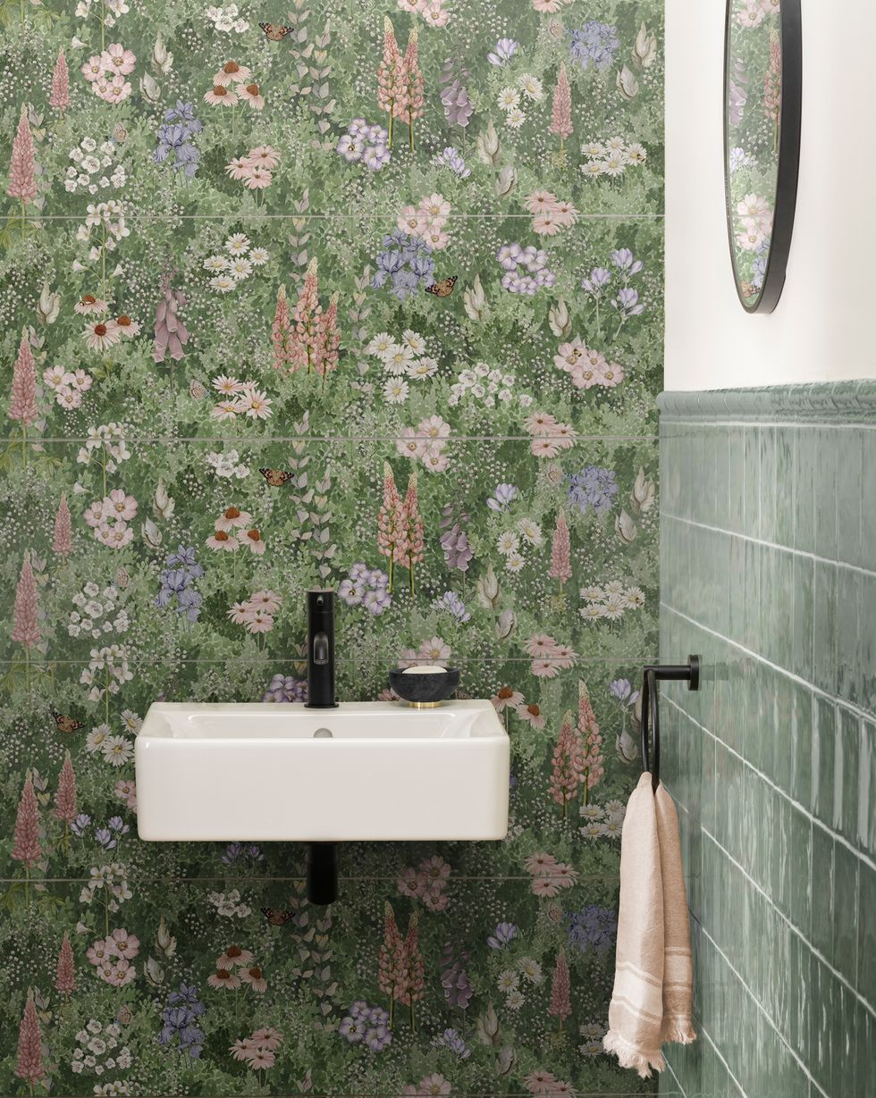 a small bathroom with floral tiles on one wall, plain green tiles on the other wall and a small white sink
