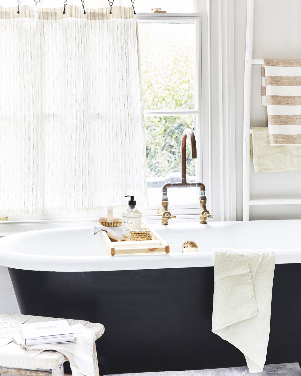 a small bathroom painted white with sheer white curtains and a black and white freestanding bath tub