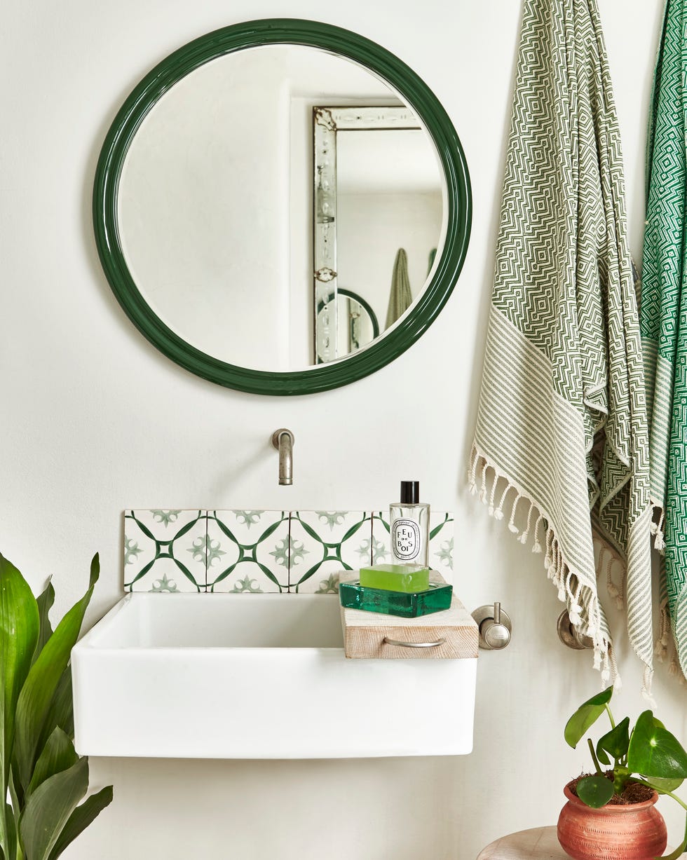 a small bathroom painted white with a wall mounted sink, green and white tiles and a round green mirror