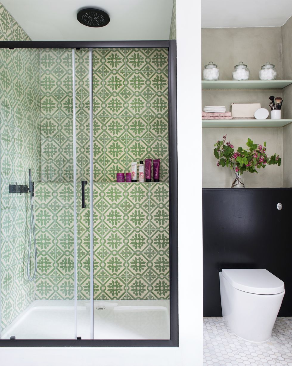 a small bathroom with green tiled shower and a recessed toilet with nook shelving above