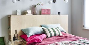 a small bedroom with wooden bed, pink bedding and glass bedside table