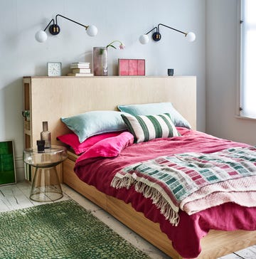 a small bedroom with wooden bed, pink bedding and glass bedside table