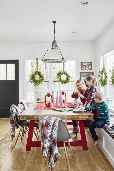 a family crafts at a table that is topped with red lanterns and red and white twine christmas trees in varying sizes