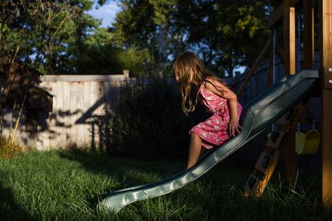 a small girl slides on a playset in her backyard at sunset