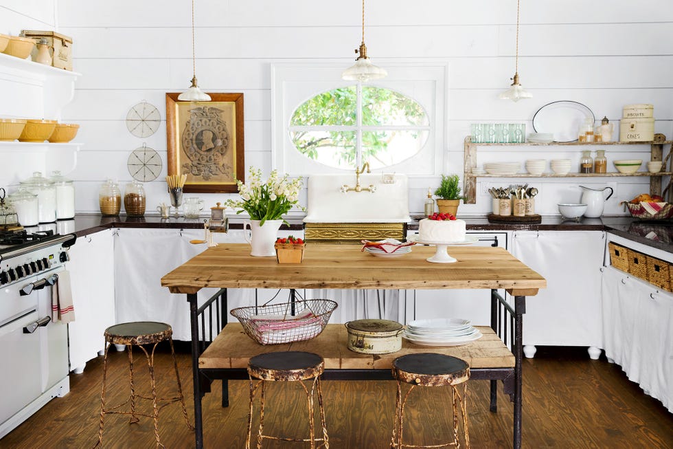a spacious kitchen with white shiplap walls and wooden flooring and a large wooden table surrounded by three stools