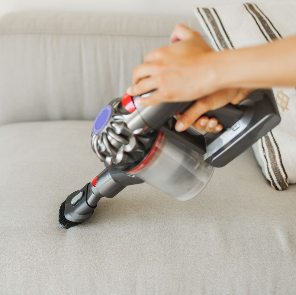 small portable vacuum cleaner in woman hands vacuuming dust on sofa