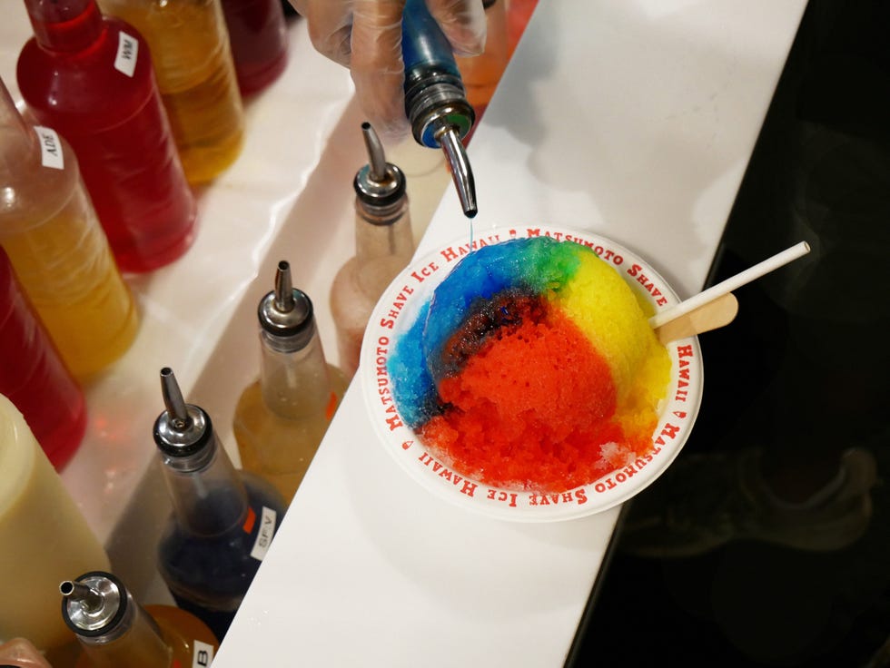 a bowl of colorful shave ice being topped with syrup